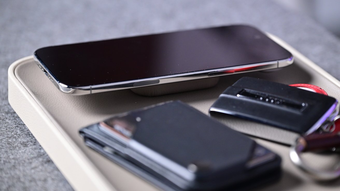 Smartphone, wallet, car key fob and key fob neatly arranged on a small tray placed on a gray fabric surface