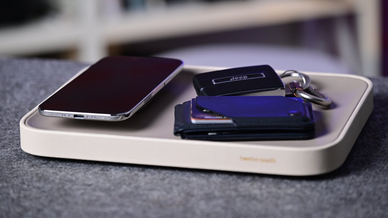 Rectangular tray on a gray surface holding a smartphone, a set of keys with fobs, and a small blue wallet, suggesting an organized spot for everyday carry items