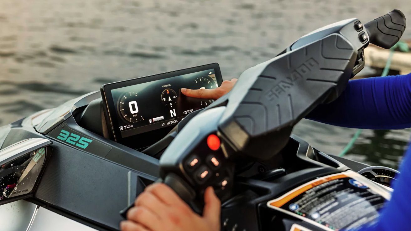 Person operating a modern jet ski, one hand on the handlebars and the other touching a large digital dashboard displaying speed, compass, and gauges, with calm water in the background