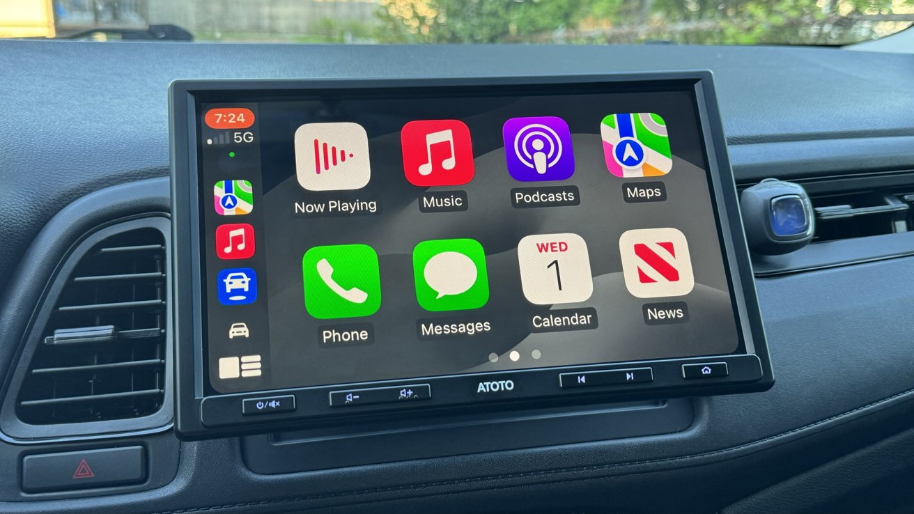 Car dashboard with a large touchscreen running Apple CarPlay, showing colorful app icons like Music, Maps, Phone, Messages, Podcasts, Calendar, and News, with surrounding air vents and controls