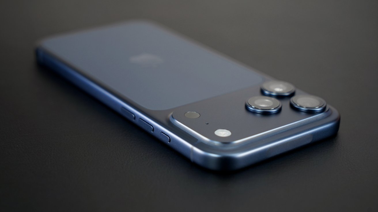 Blue smartphone lying face down on a dark surface, showing triple rear camera bump, side buttons, and sleek metallic edges in soft, angled lighting