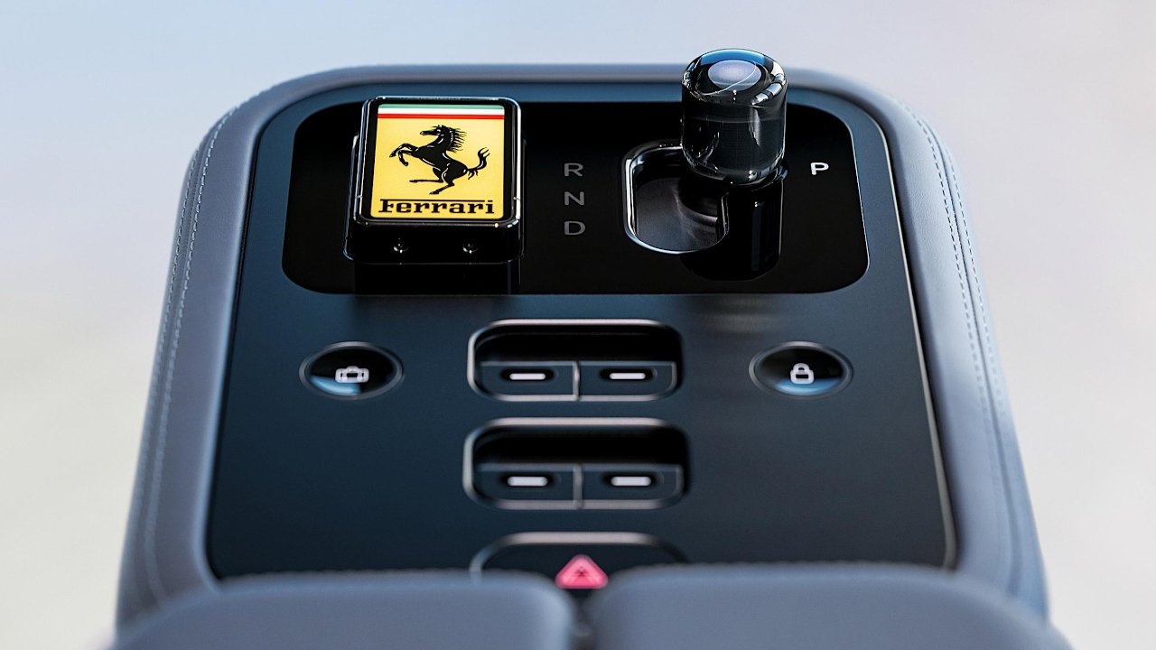 Ferrari car center console showing yellow prancing horse logo, glossy black gear selector with R N D and P positions, and surrounding buttons for window and door lock controls