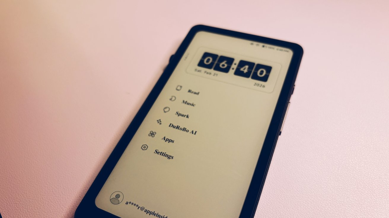 Смартфон с дисплеем в стиле электронных чернил на пастельной поверхности показывает большие раскладные часы в 06:40 и вертикальное меню приложений, включая «Чтение», «Музыка», «Spark», Durobo AI, «Приложения», «Настройки».