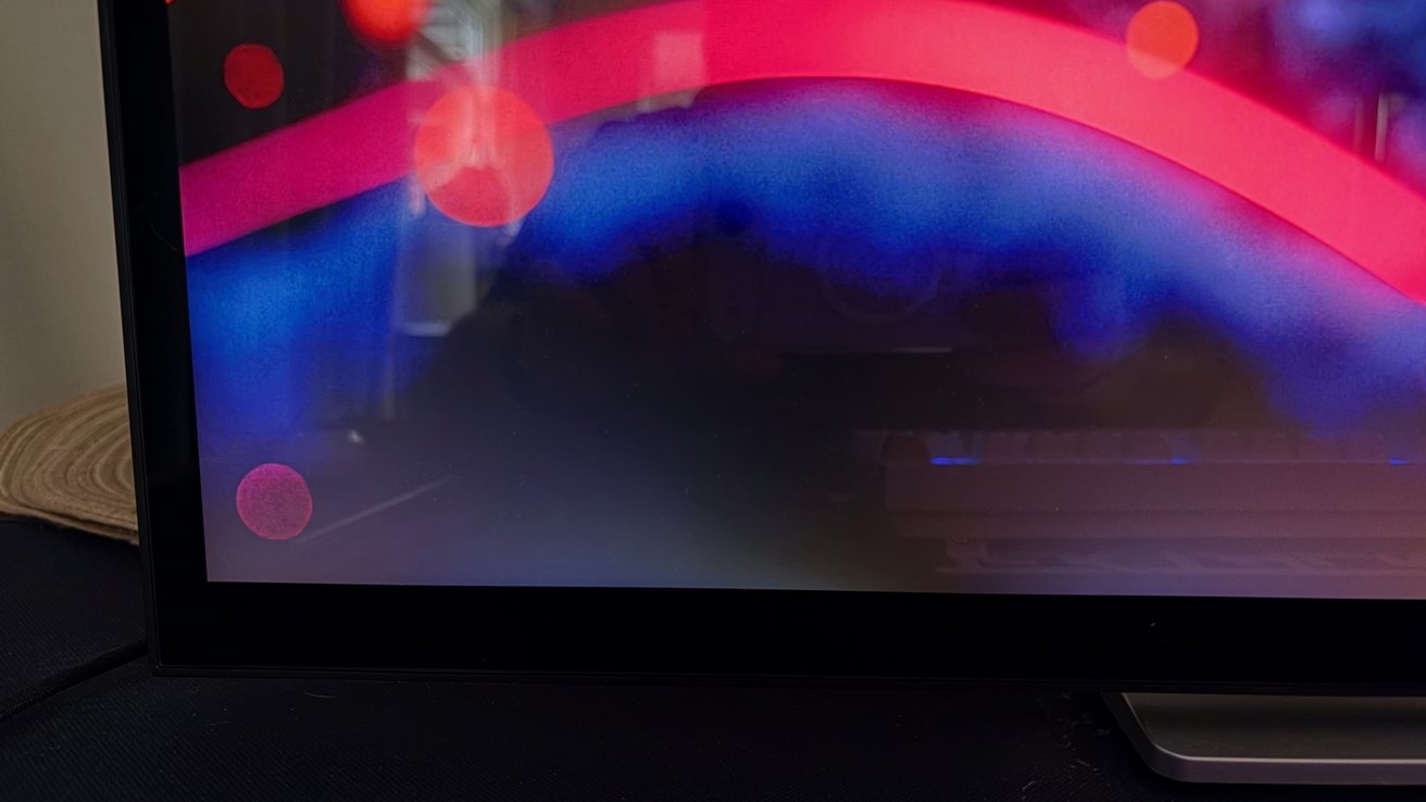 Monitor screen displaying abstract digital art with a bright red arc, soft blue gradient background, and several glowing red circles, reflected faintly on a dark glossy surface