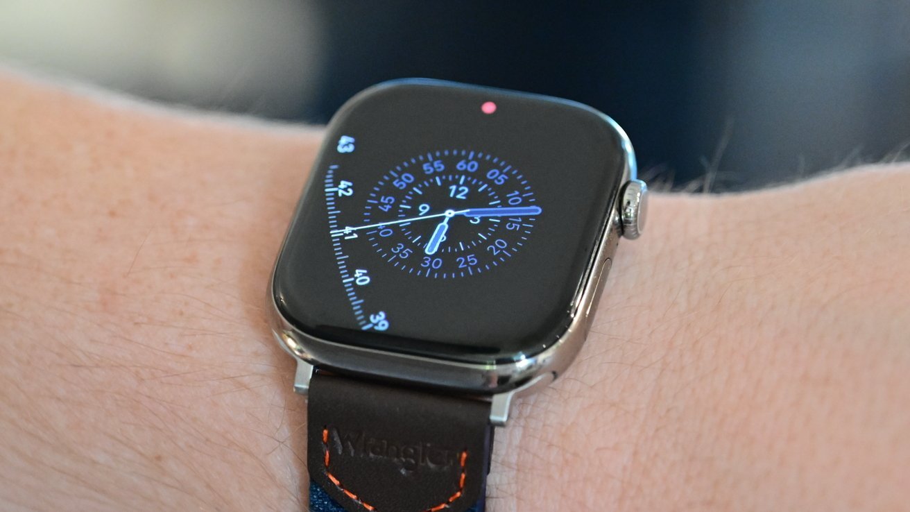 Apple Watch Series 11 on the wrist with a blue analog-style dial with numbers and markers, housed in a silver case with a dark leather band and orange stitching