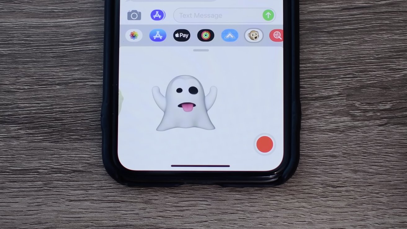 Smartphone on wooden table with text message screen with playful white ghost emoji sticking out tongue and red circular record button in corner