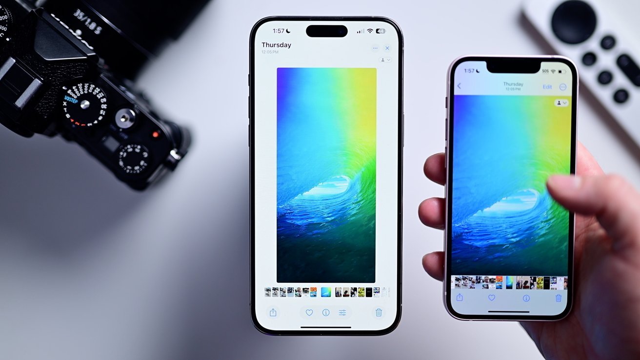 Two iPhones side by side display a color photo of sea waves while a hand holds the correct phone; the camera and remote control remain blurred in the background on a white surface