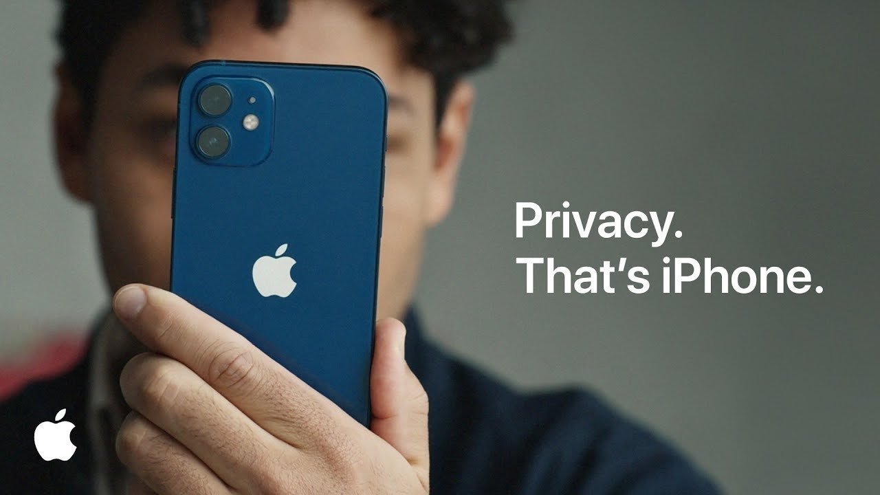 Person holding a blue iPhone close to their face, Apple logo visible, with text on the right reading Privacy. That's iPhone on a plain gray background