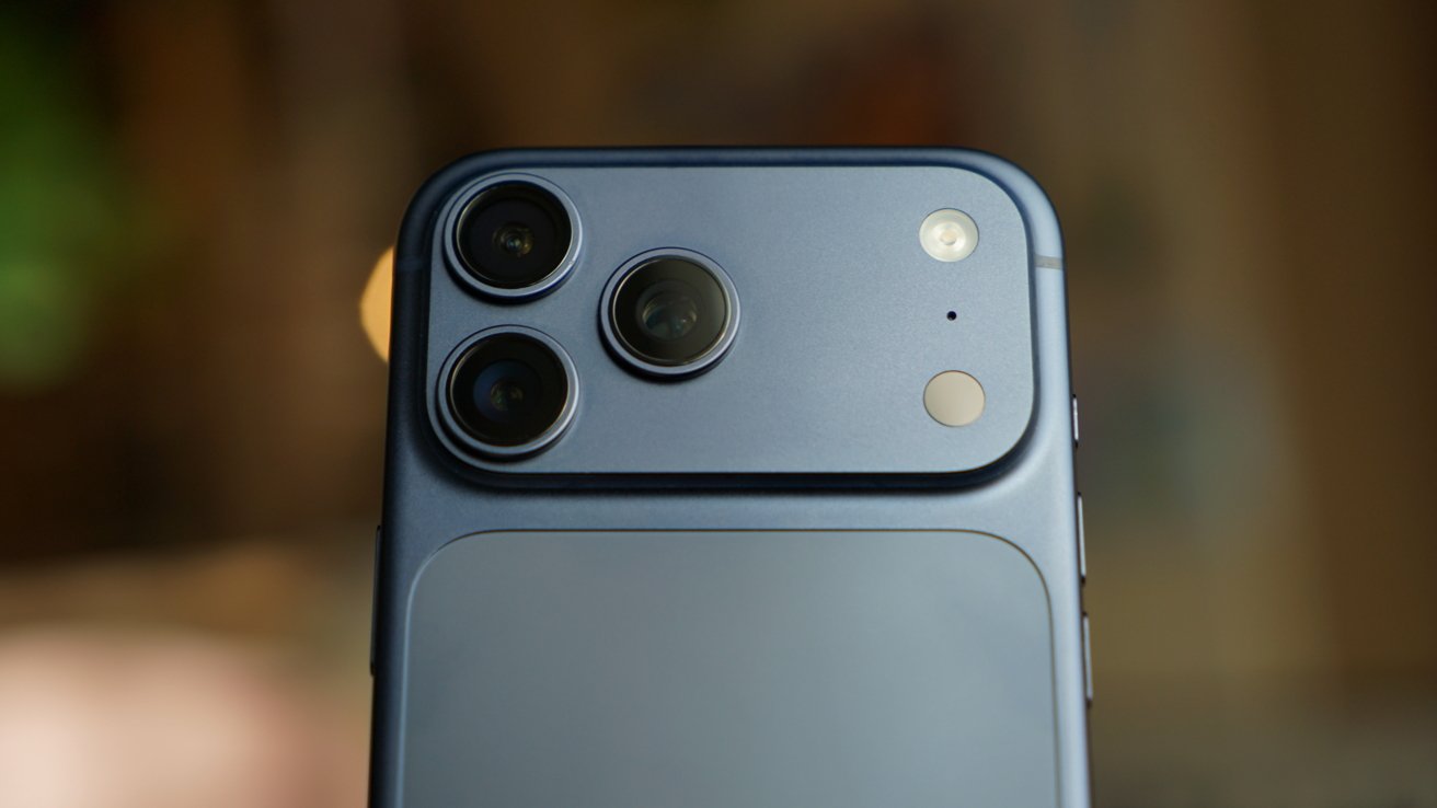 Close-up of a blue iPhone 17 Pro Max back, showing three rear camera lenses, flash, and sensors on a rectangular camera bump against a softly blurred background