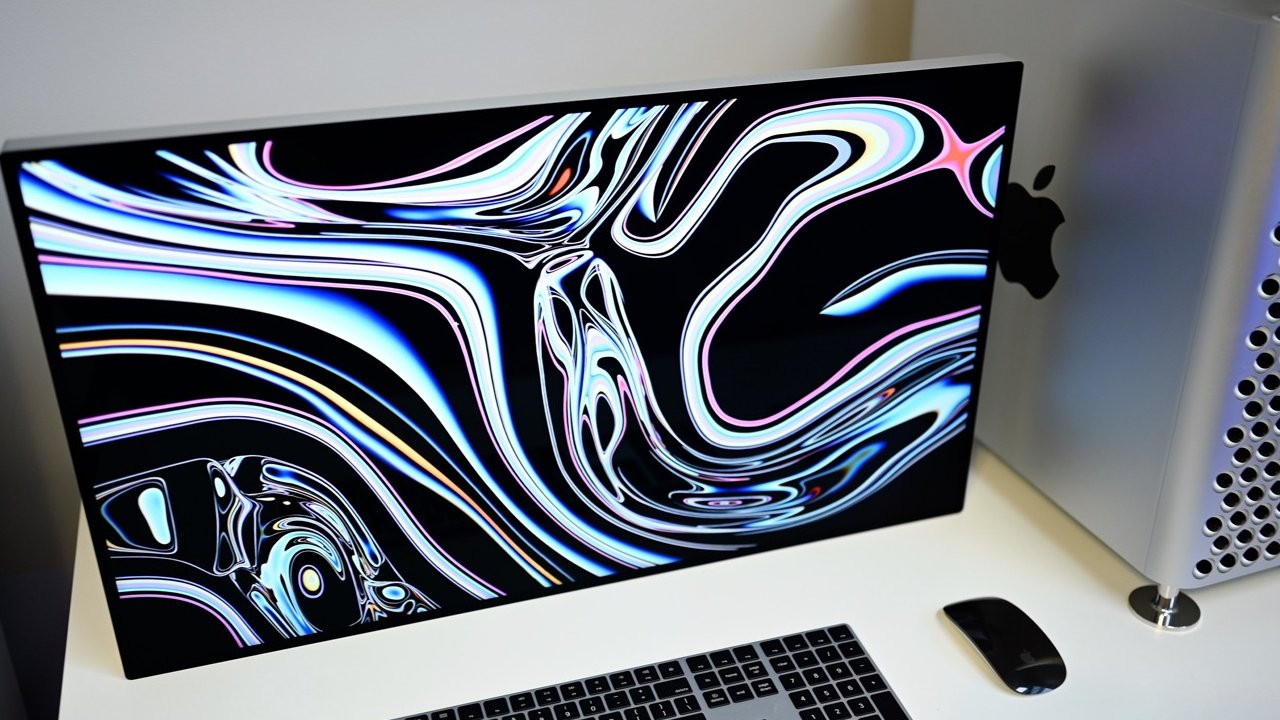 Large desktop monitor with colorful swirling abstract pattern on screen, sitting on white desk beside a silver computer tower, black keyboard, and black wireless mouse.