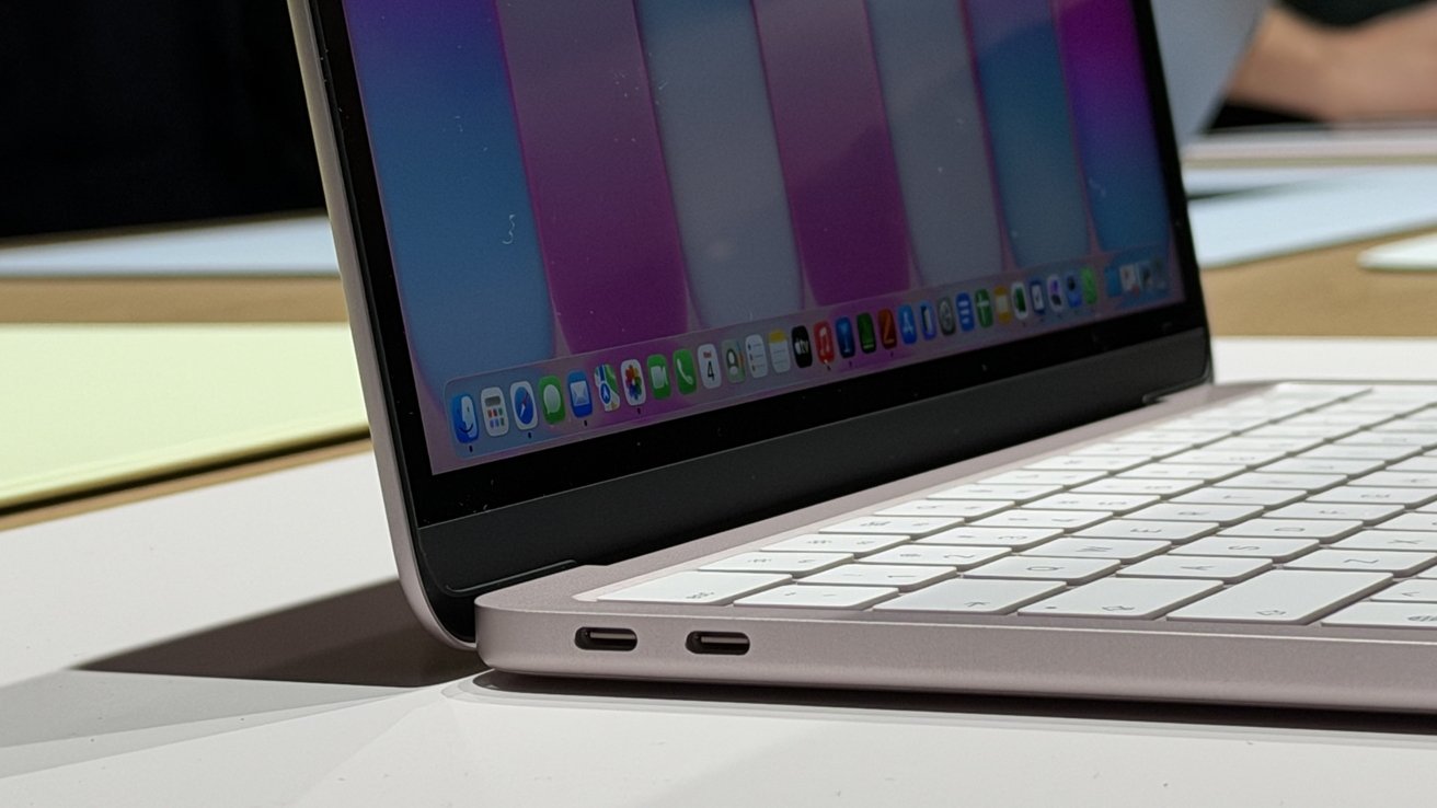 Side view of an open slim laptop with white keyboard, colorful desktop screen, and two USB-C ports on the left edge, resting on a glossy table in a bright room