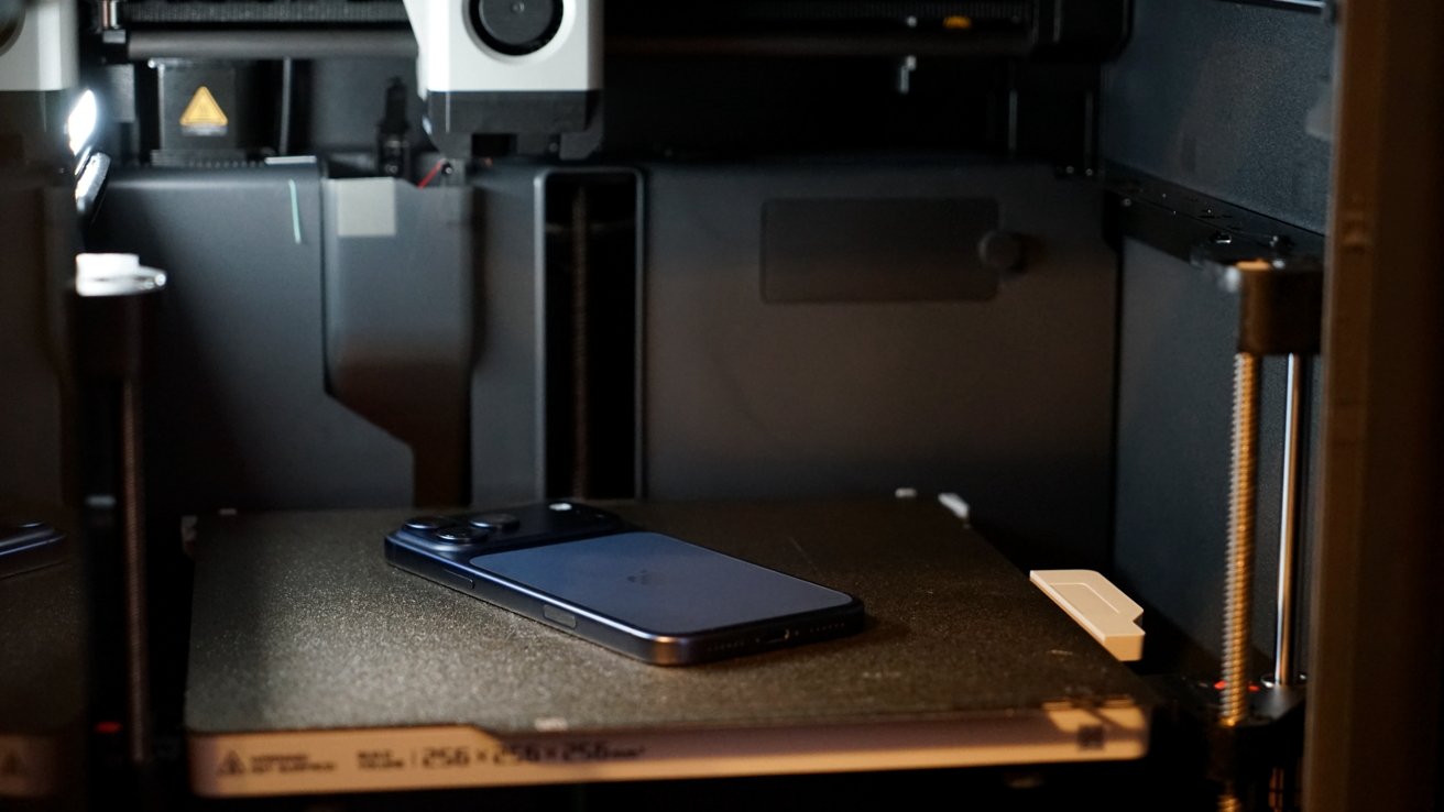 A blue iPhone 17 Pro Max laying facedown in a 3D printer bed