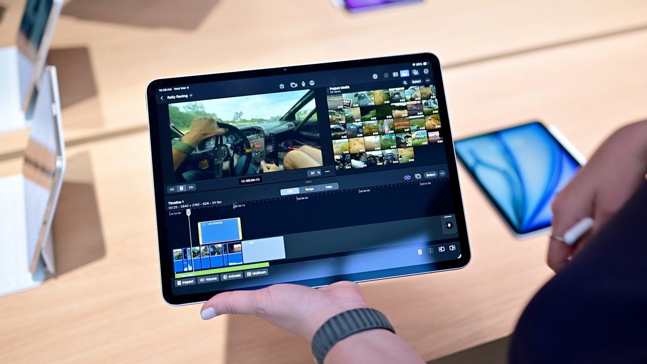 Person holding a tablet on a store counter, editing a racing video with multiple clips and timelines on screen, surrounded by other display devices in the background