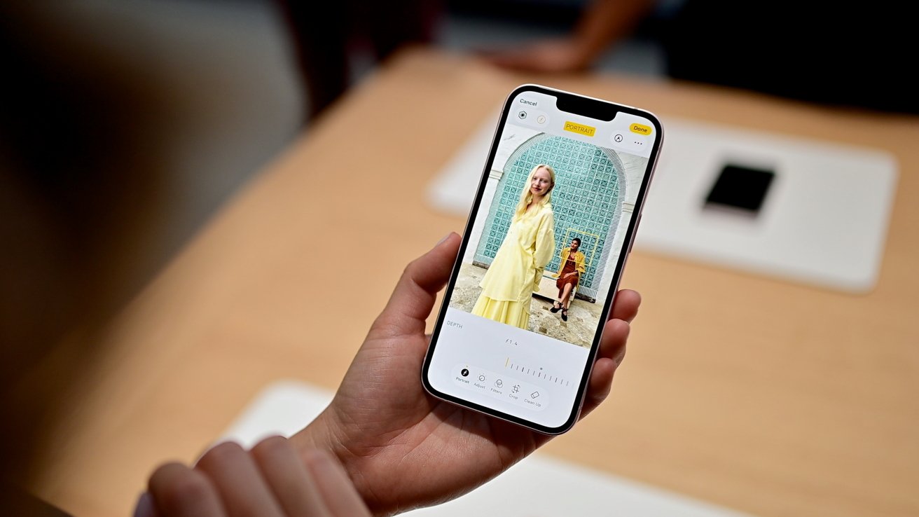 Hand holding a smartphone displaying a portrait photo of two women posing by a decorative tiled arch, with on-screen camera controls and editing options visible at the bottom