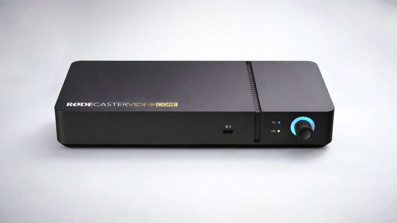 Black rectangular RODECaster Duo audio device on a light background, featuring a small power switch and a circular control knob with a glowing blue ring on the front panel