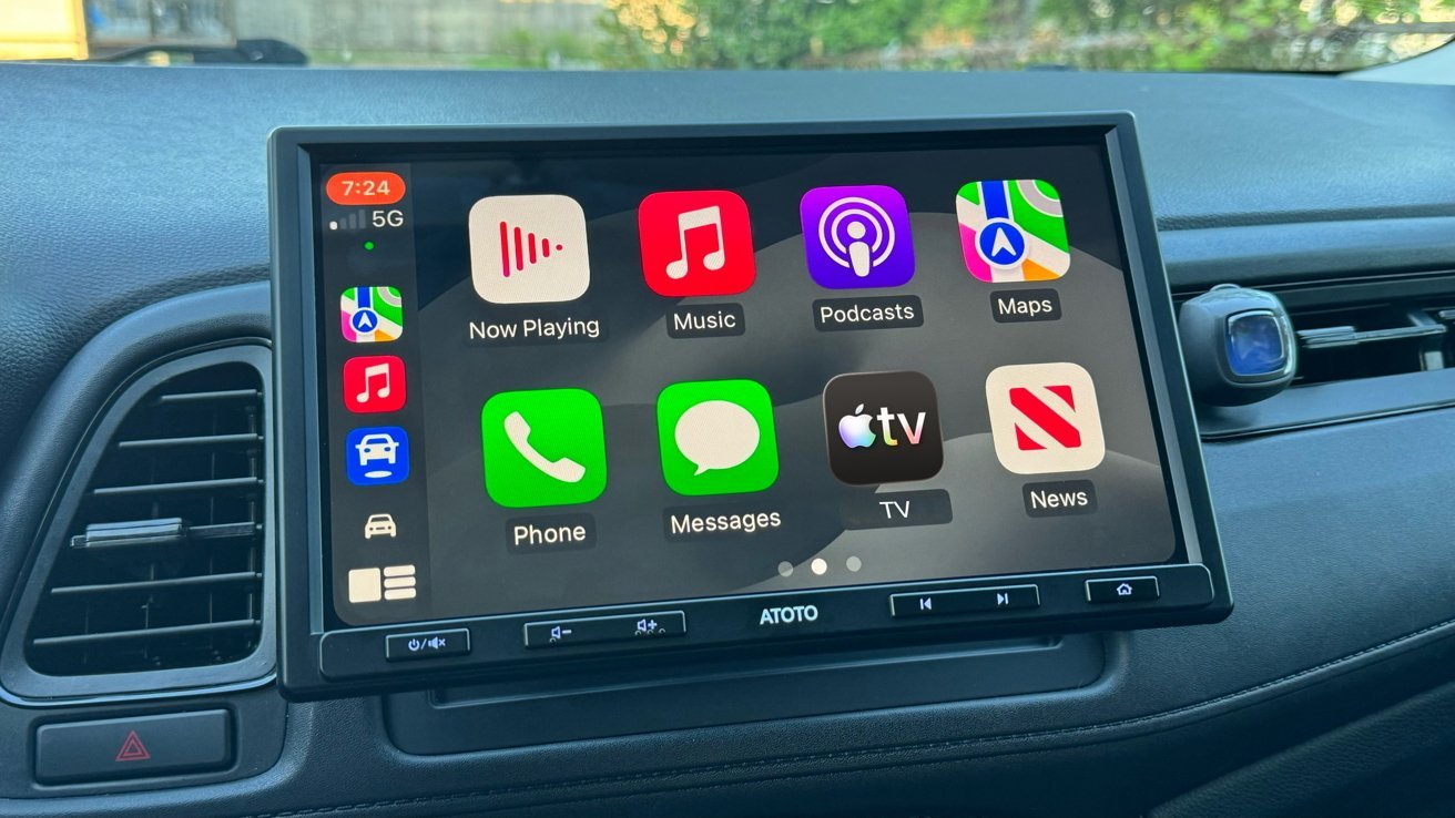 Car dashboard with large touchscreen showing Apple CarPlay home screen, including apps for Music, Podcasts, Maps, Phone, Messages, TV, and News, with vents and controls around the display