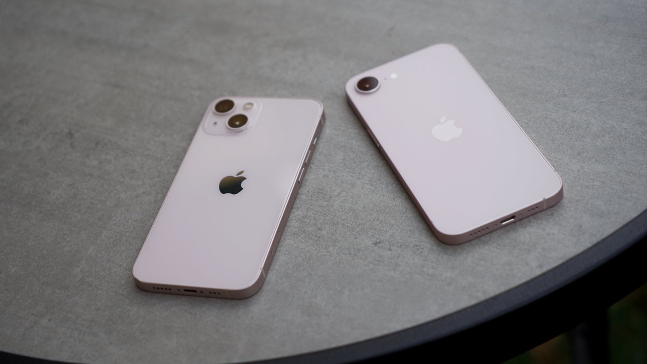 Two light pink iPhones lying face down on a round gray table, one with dual rear cameras and the other with a single camera, both showing the Apple logo