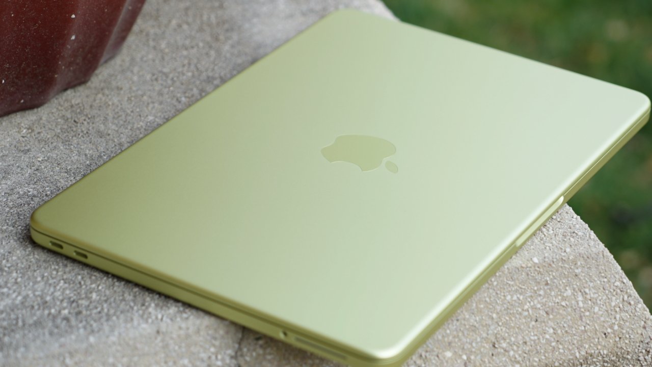 Closed light green Apple laptop resting on a textured concrete surface outdoors, showing the Apple logo on the lid and thin edges with visible side ports