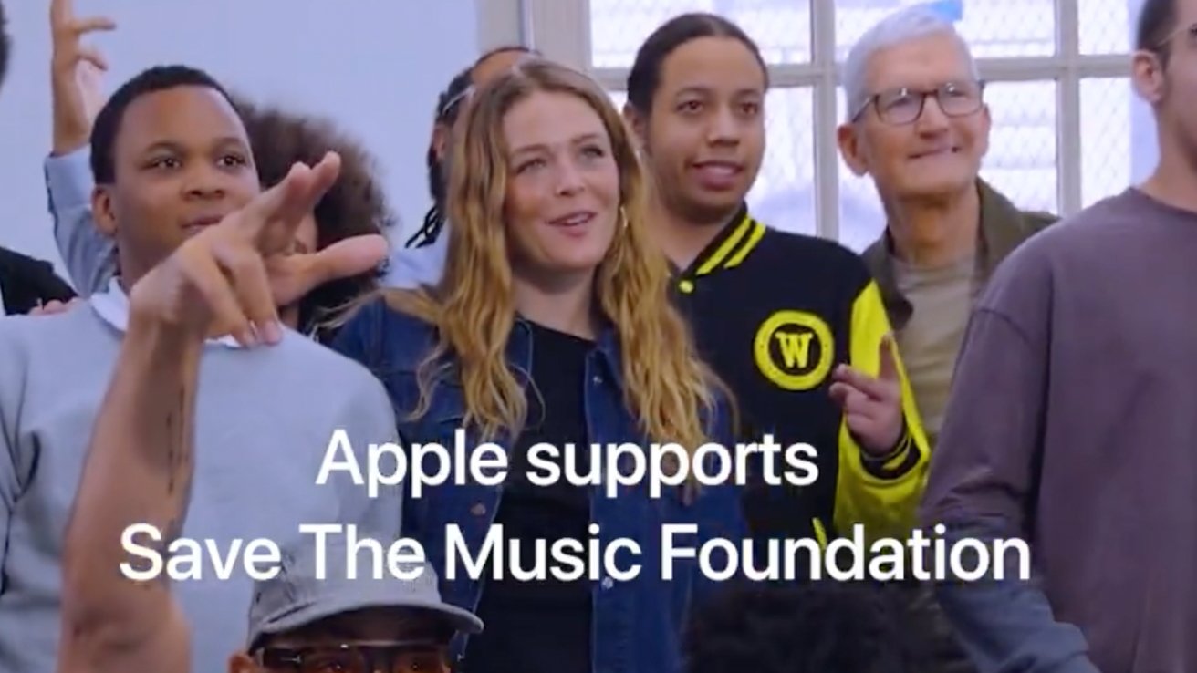Diverse group of smiling people standing together indoors, some gesturing enthusiastically, with overlaid white text reading Apple supports Save The Music Foundation