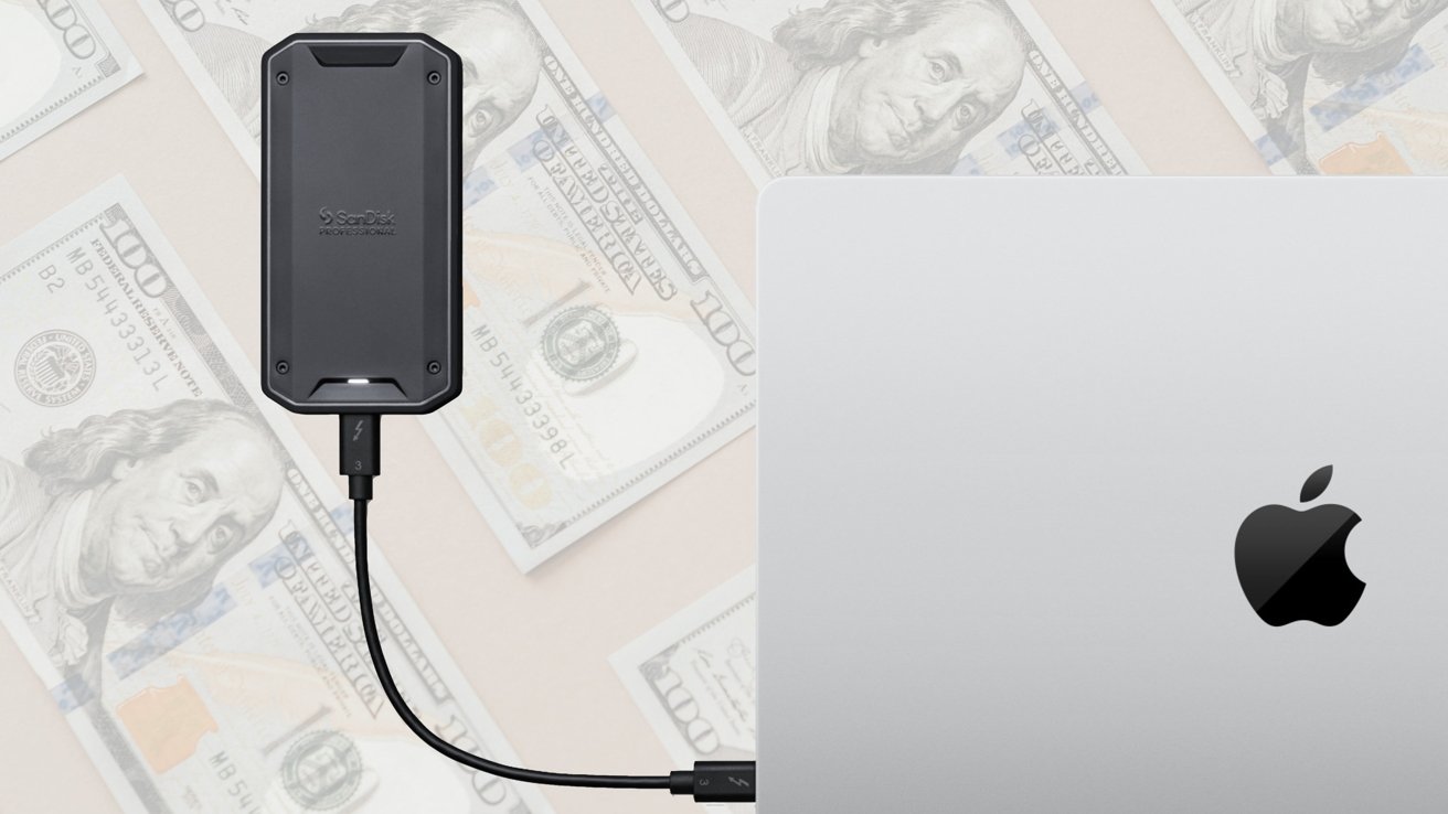 External SanDisk Professional drive connected by cable to a silver MacBook with Apple logo, lying over scattered US hundred dollar bills in the background