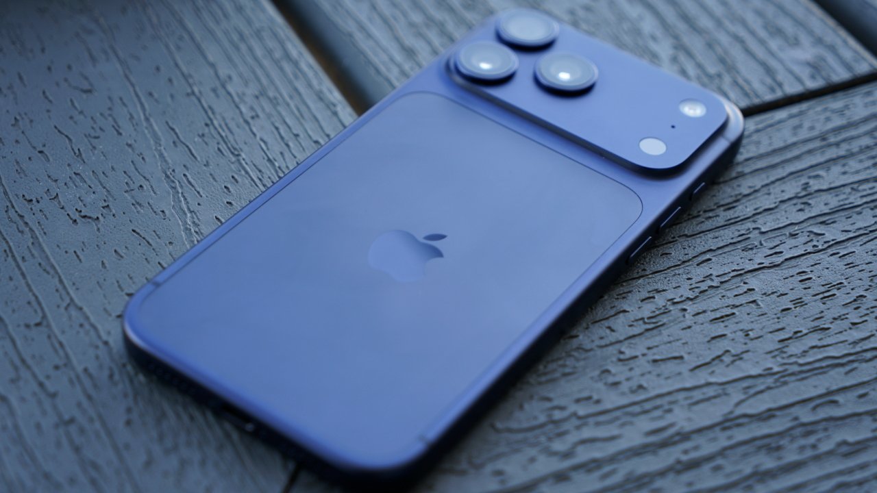 Blue iPhone lying face down on textured dark wooden surface, showing Apple logo and three raised rear camera lenses in the top corner