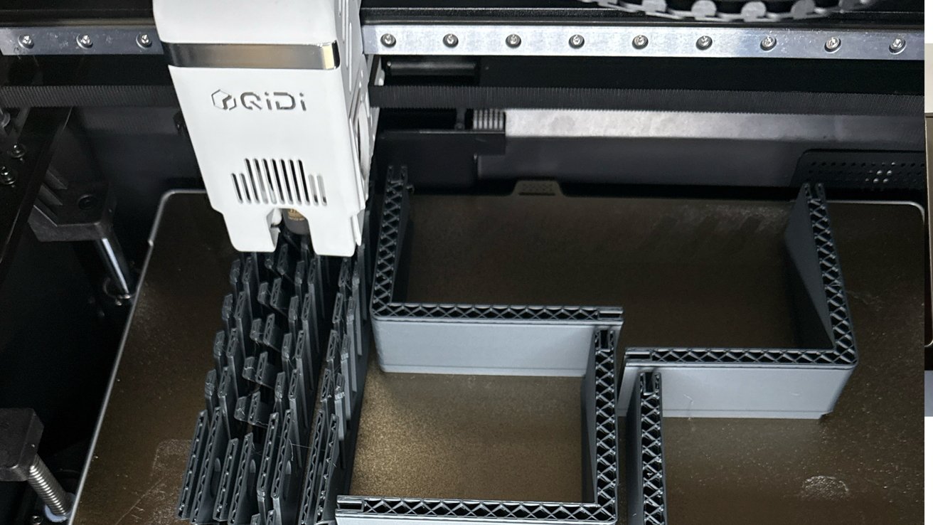 QIDI 3D printer head actively printing large gray plastic parts with lattice infill, forming angular walls and support structures on the printer's build plate
