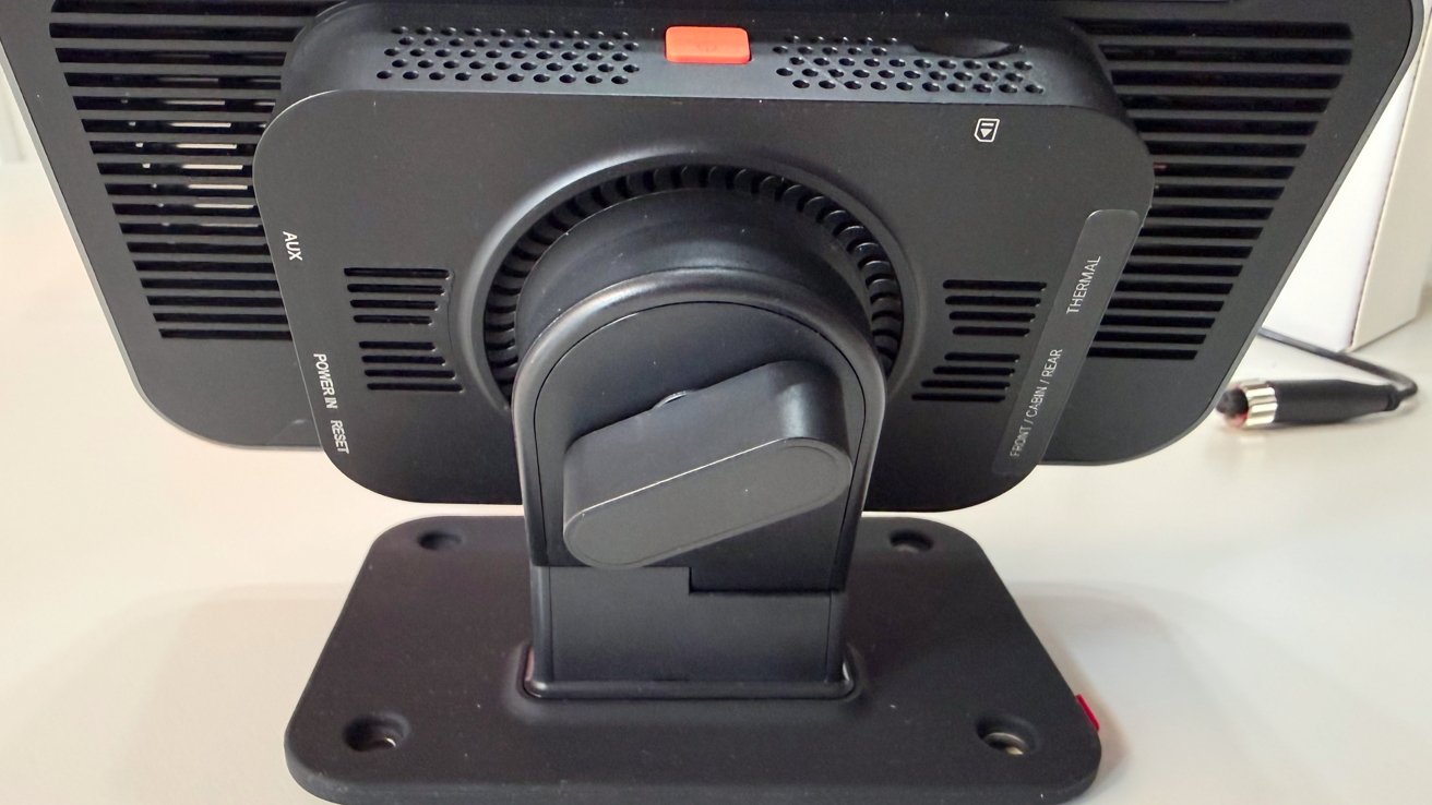 Rear view of a black monitor on a sturdy rectangular stand, showing the central swivel hinge, ventilation slots, labeled ports, and a small red button on the top edge.