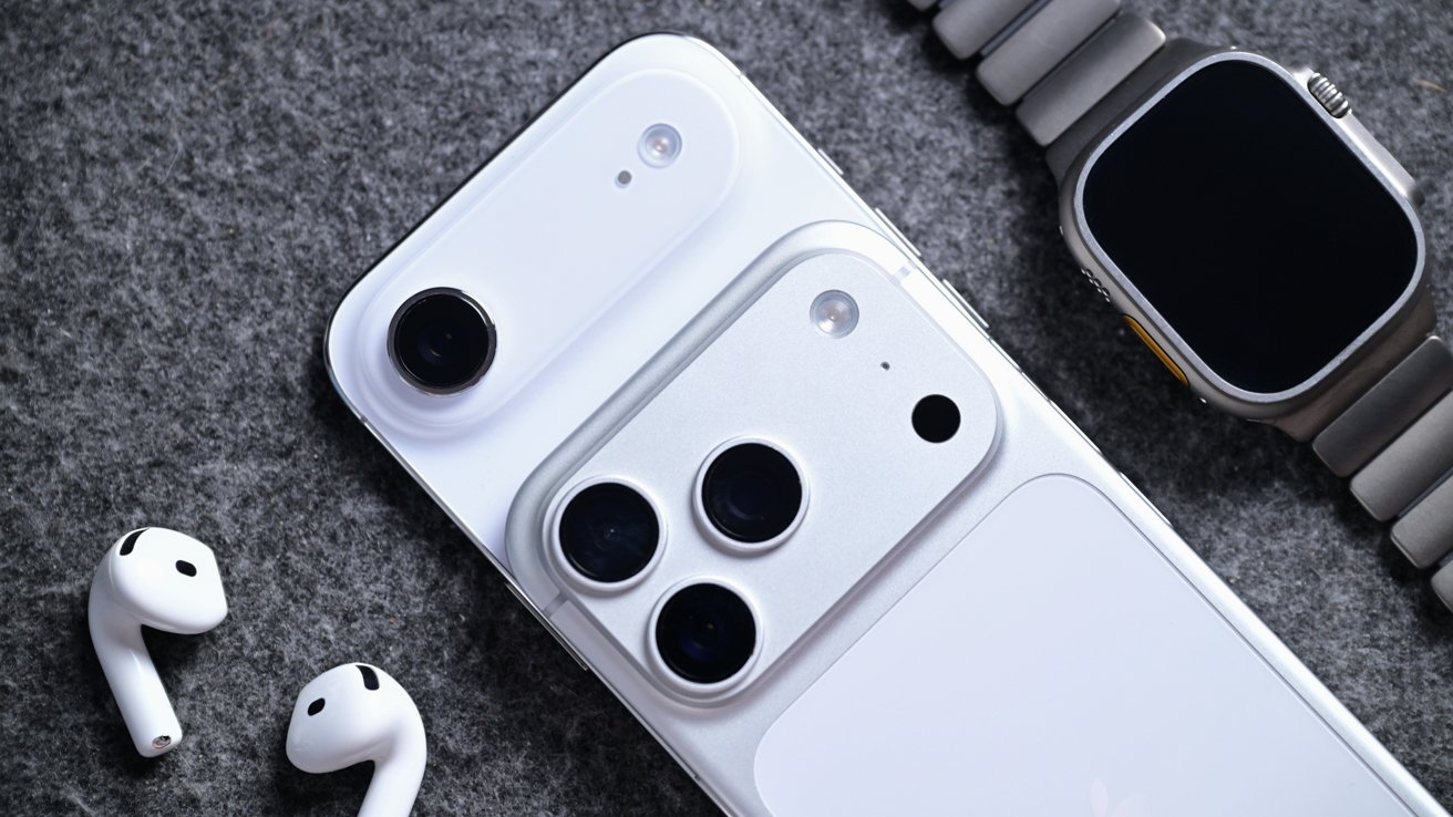 Close-up of two white smartphones with prominent rear cameras, a metal smart watch with dark screen, and a pair of white wireless earbuds on a gray fabric surface