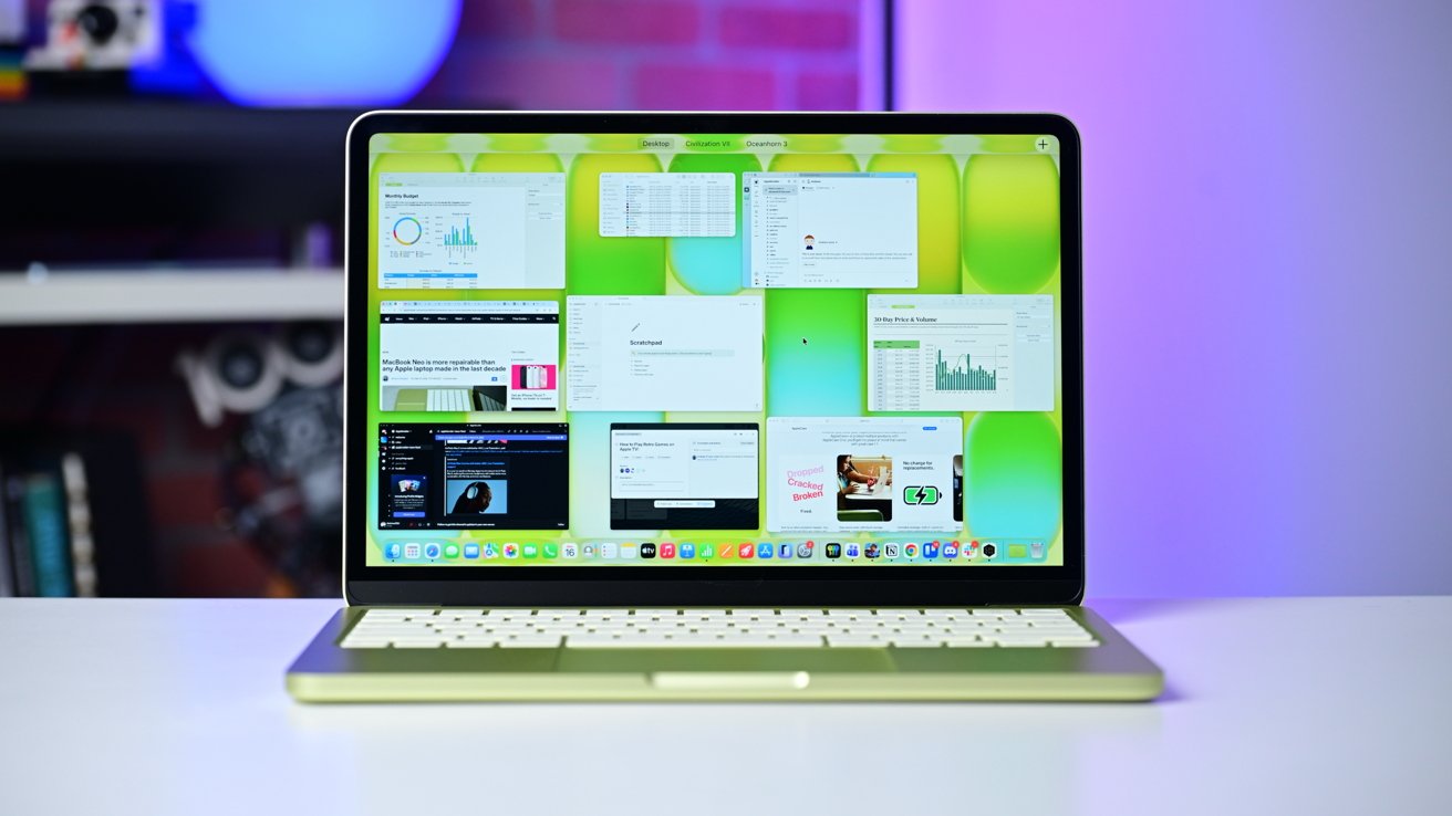 Open MacBook on a desk showing Mission Control with multiple app windows over a bright green abstract wallpaper; blurred shelves and purple lighting in the background