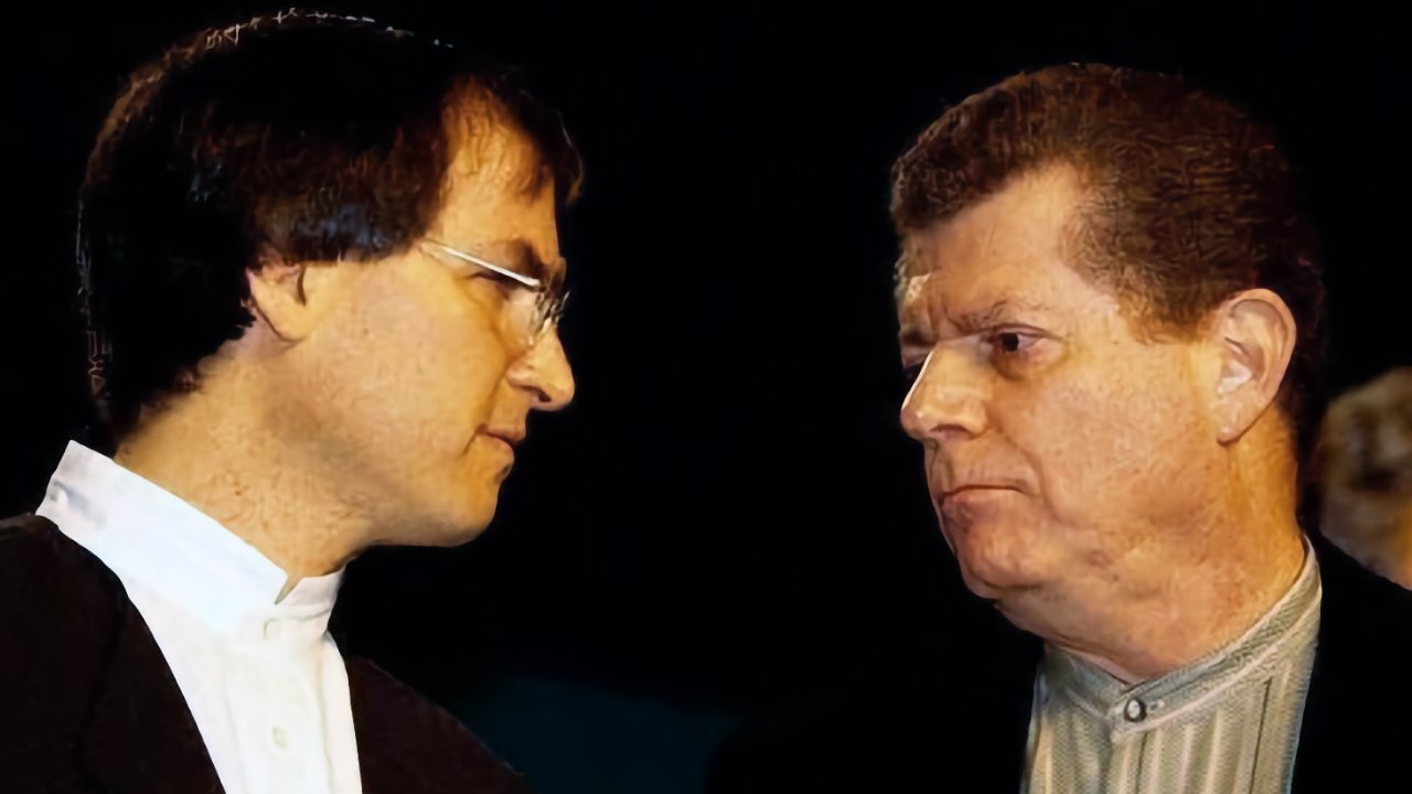 Two middle-aged men stand close, facing each other seriously against a dark background, both in formal clothing, appearing to be in an intense or thoughtful conversation