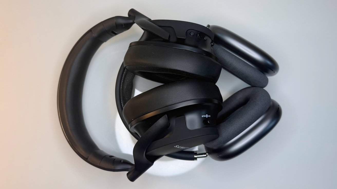 Two pairs of large over-ear headphones, black with cushioned ear cups, stacked and intertwined on a light gray surface, viewed from above