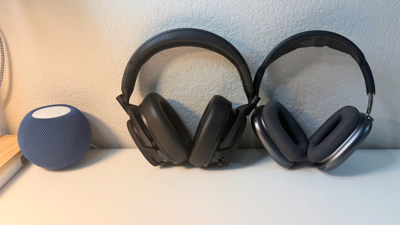 Blue smart speaker and two over-ear headphones resting side by side on a white desk against a light textured wall