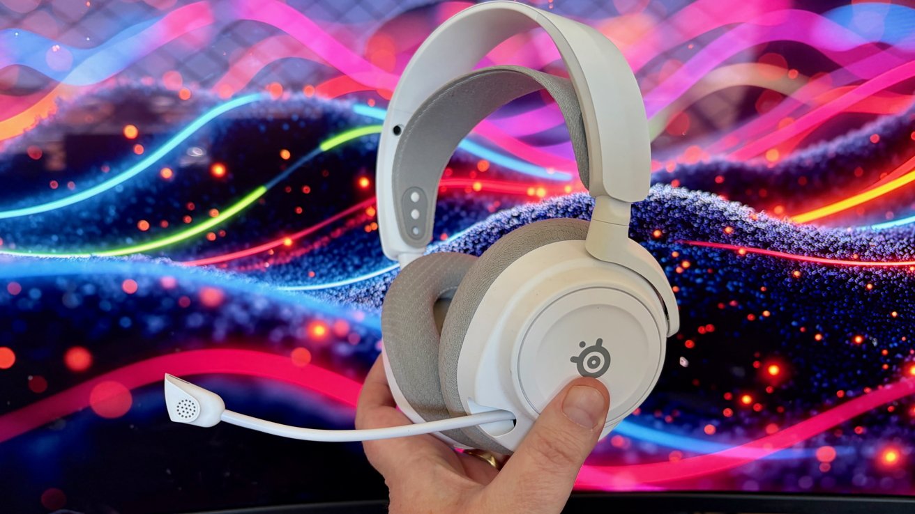 Hand holding white gaming headset with attached microphone in front of a colorful, abstract neon background of wavy light streaks and glowing dots