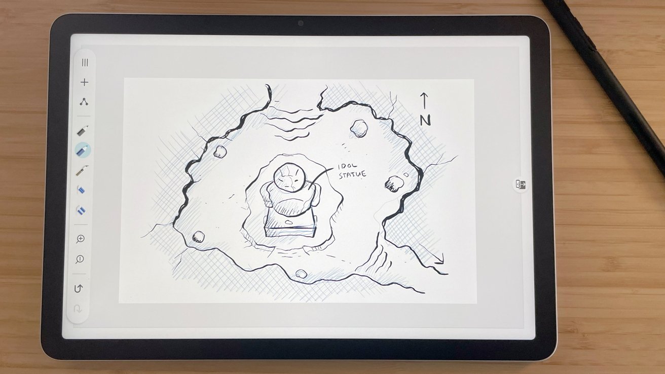 Tablet on wooden desk displaying a sketch of a rocky cave with a central idol statue labeled Idol Statue, drawn in black ink with shading and scattered rocks.