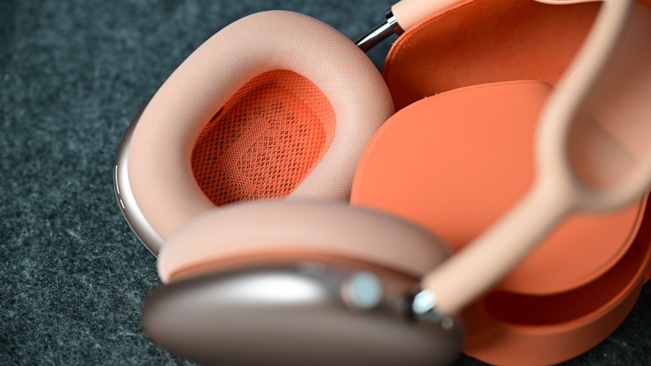 Close-up of peach and orange over-ear headphones with soft mesh ear cushions resting on a textured dark gray surface