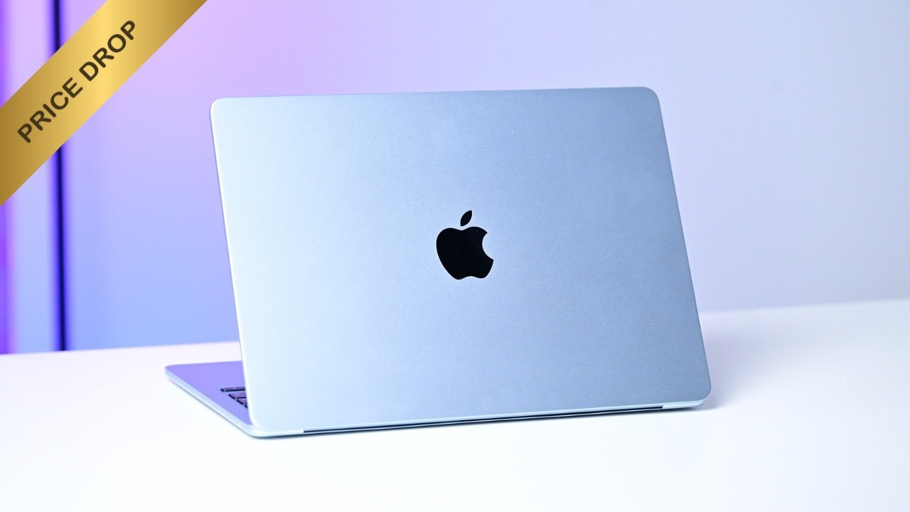 Silver Apple MacBook laptop on a clean white desk, lid closed, Apple logo centered, with a yellow diagonal banner in the top-left corner reading PRICE DROP