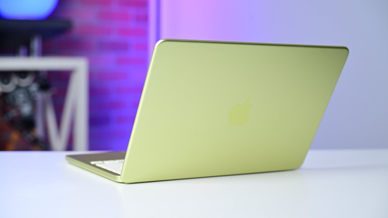 Slim yellow-green laptop partially open on a white desk, viewed from behind, with blurred colorful background lighting and modern room decor out of focus