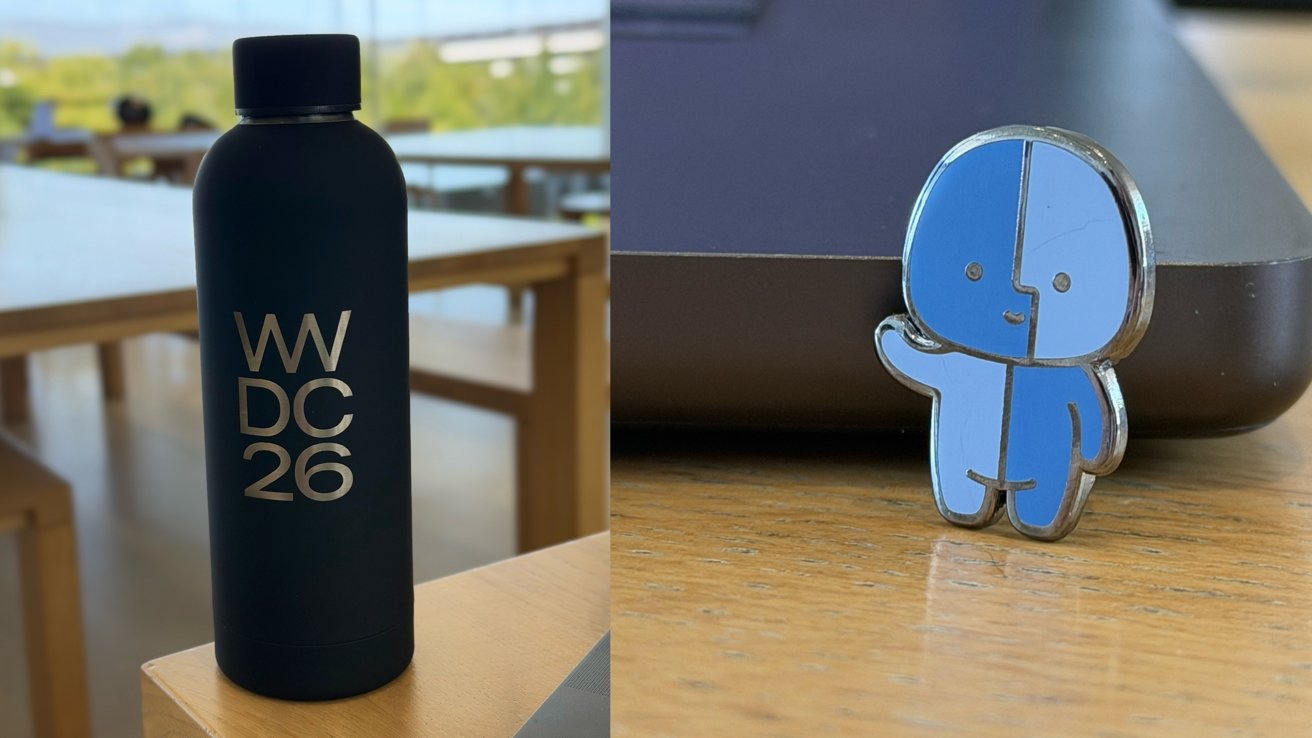 Black water bottle labeled WWDC26 on a wooden table beside a windowed workspace, next to a small blue cartoon character pin standing upright near a laptop edge